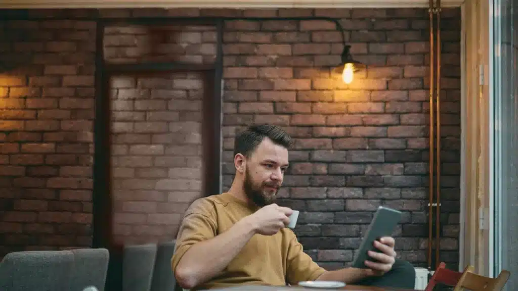 A man holding a cup of coffee while using a tablet in a café.