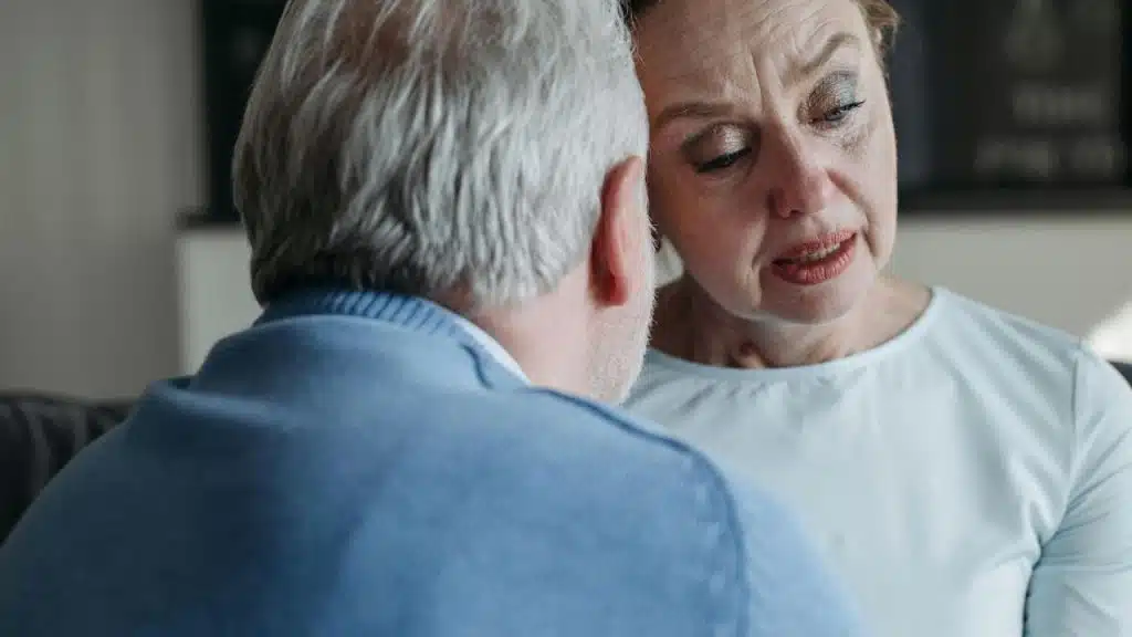 An older woman with a distressed expression rests her head against another person's gray hair.