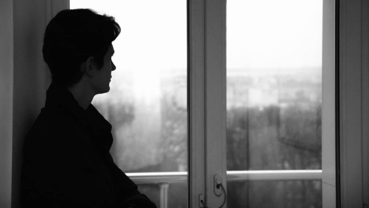 A black and white silhouette of a person looking out a window at a city.