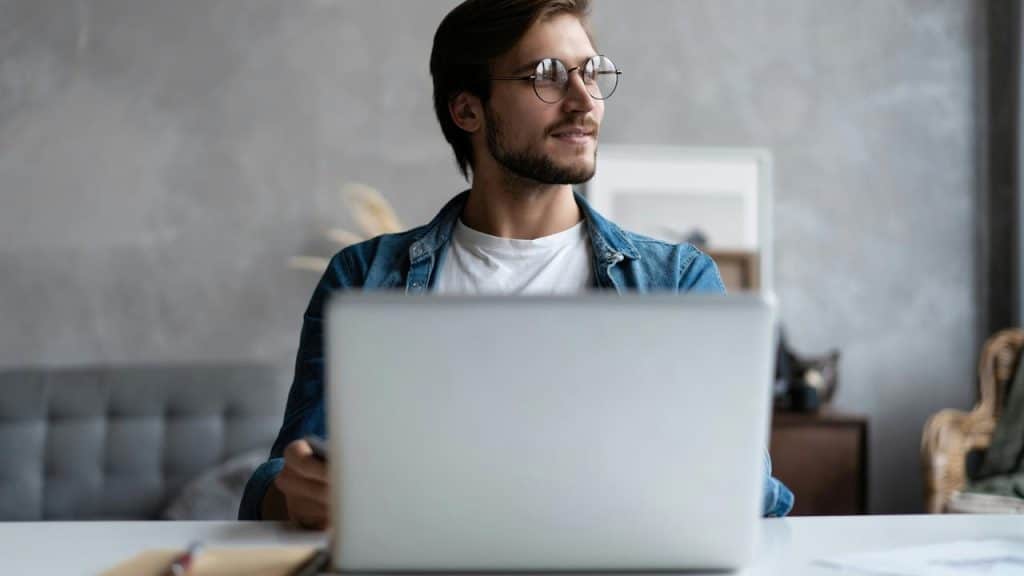 A man wearing glasses working on a laptop.