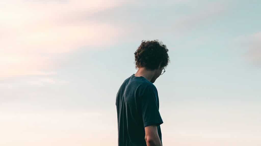 A man in a black crew-neck t-shirt standing under a white sky during daytime.