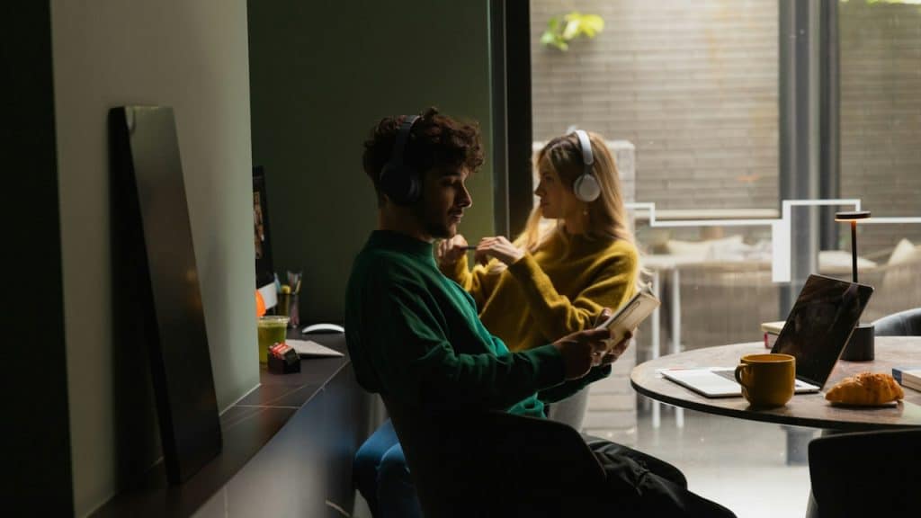 A couple wearing headphones and sitting while using their electronic gadgets and not talking.