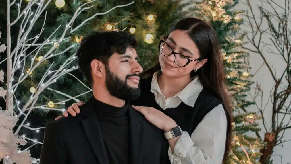 A man and woman sitting next to a Christmas tree.