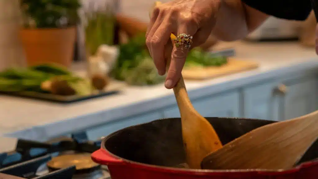 A hand stirring food in a pot on a stove.