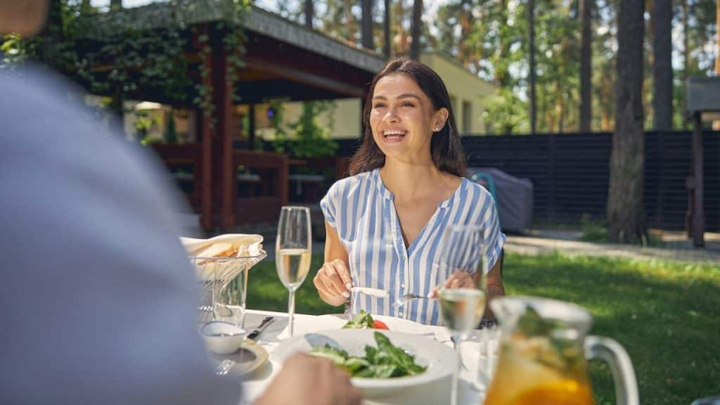 A woman in a blue-and-white striped shirt laughs while sitting at an outdoor dining table.
