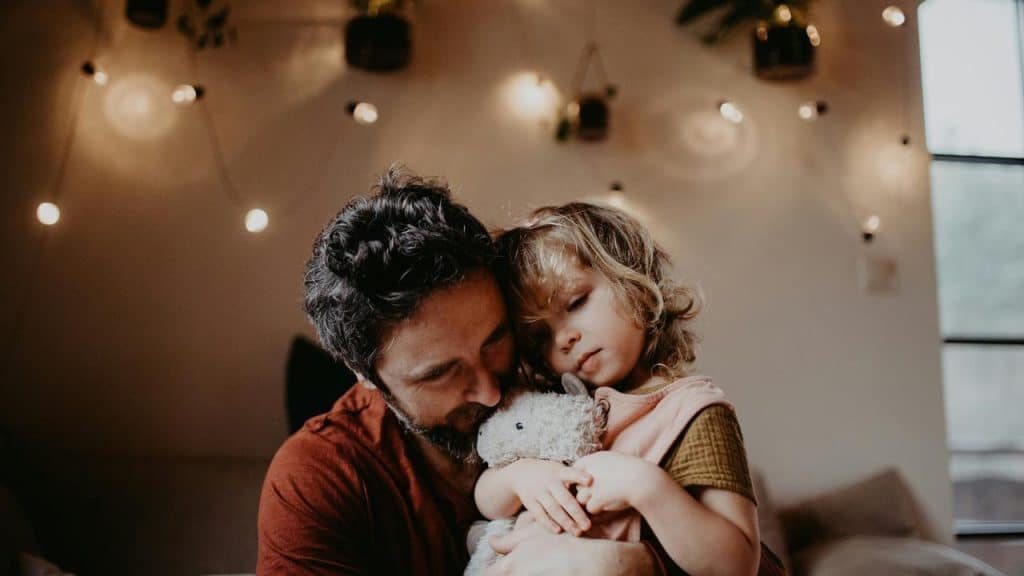 A man hugging a child holding a stuffed animal.