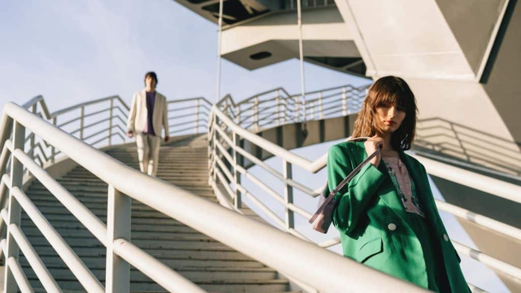 A woman in a green coat walks down outdoor stairs while a man follows behind.