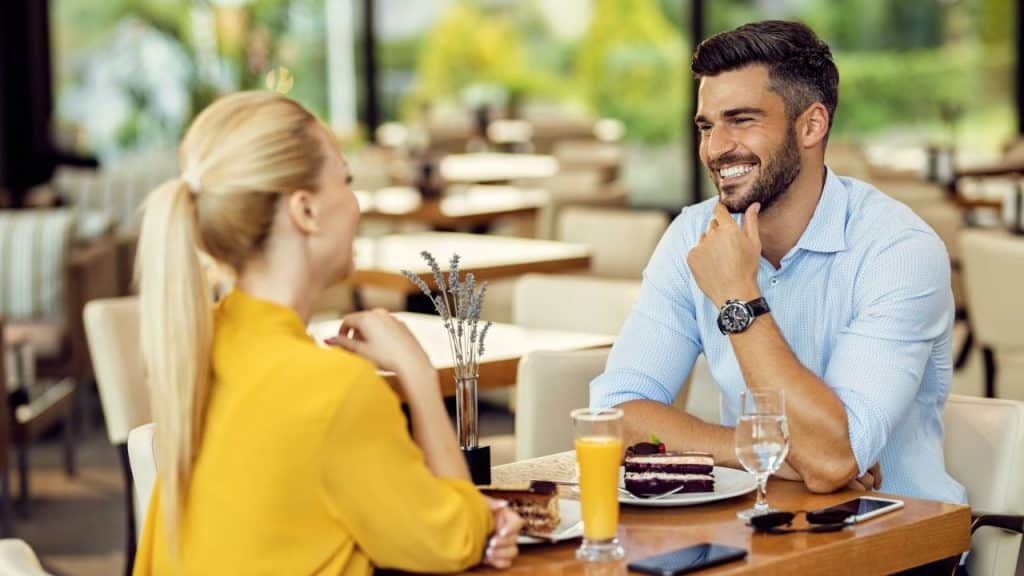 A man and woman sit at a cafe table with cake, coffee, and orange juice.