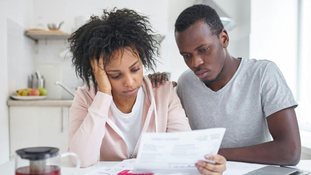 A man and woman sit together at a table looking down at a white document.