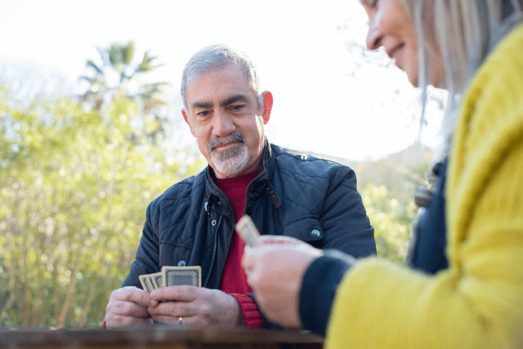 Senior couple sitting down playing cards outdoors