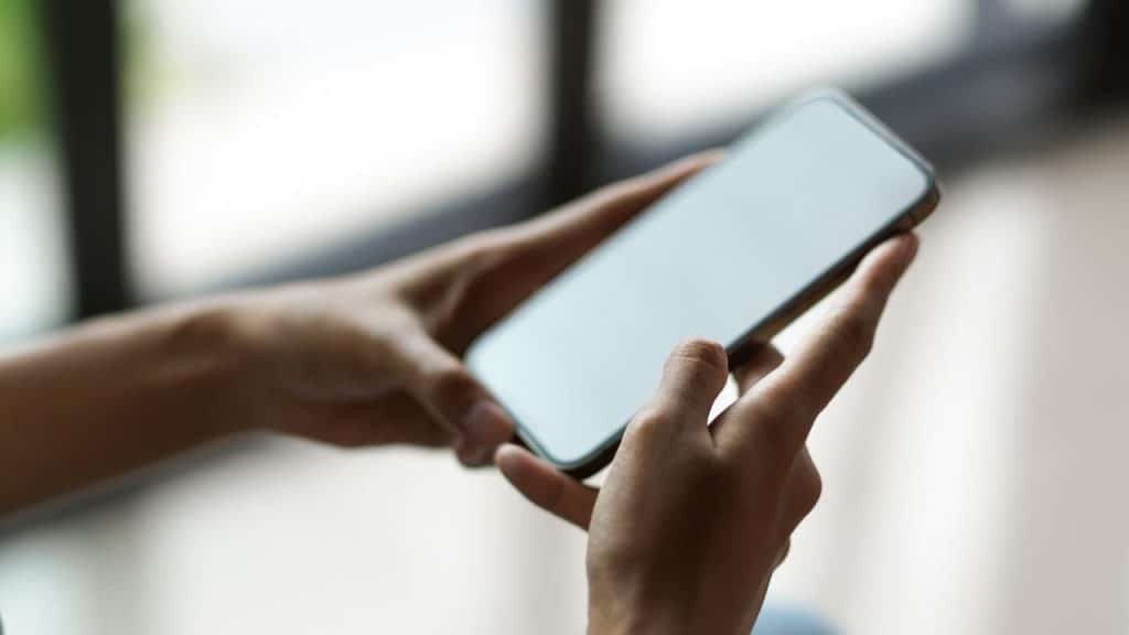 A person holding a smartphone with the screen turned off.