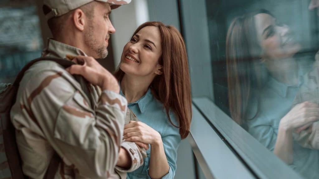 A smiling woman stands close to a man wearing a military-style camouflage uniform and cap.