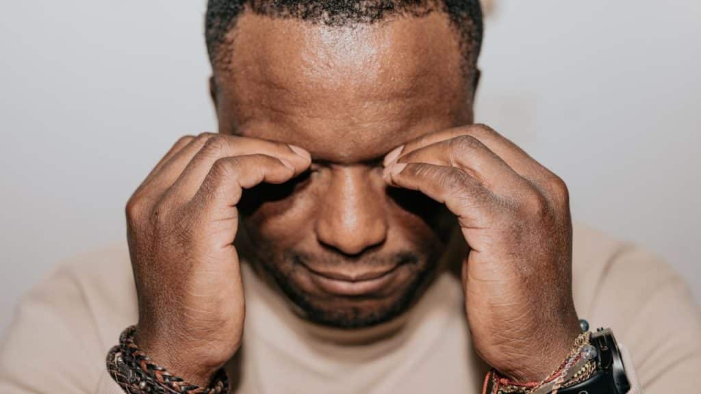 A man with eyes closed rubs the bridge of his nose with both hands.