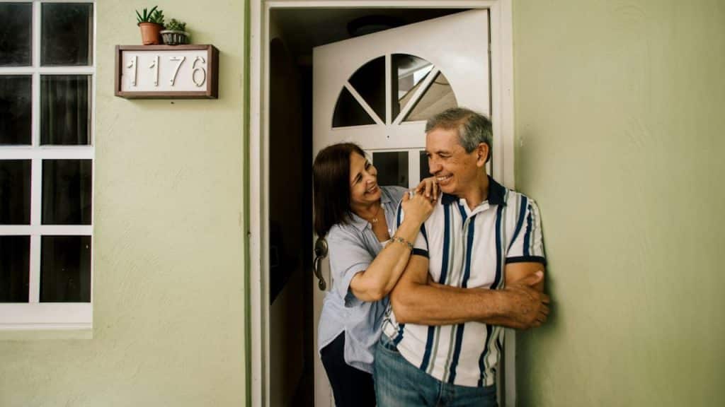 A man and woman stand by a doorway, the woman leaning on the man's shoulder.