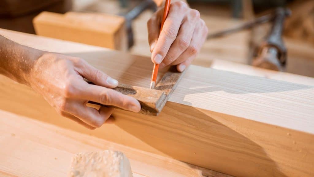 A person marking a wooden plank with a pencil and square.