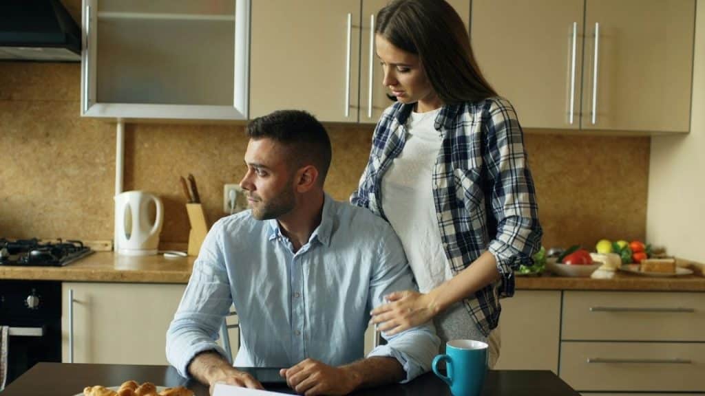 A woman in a plaid shirt stands and places her hand on a man’s arm.