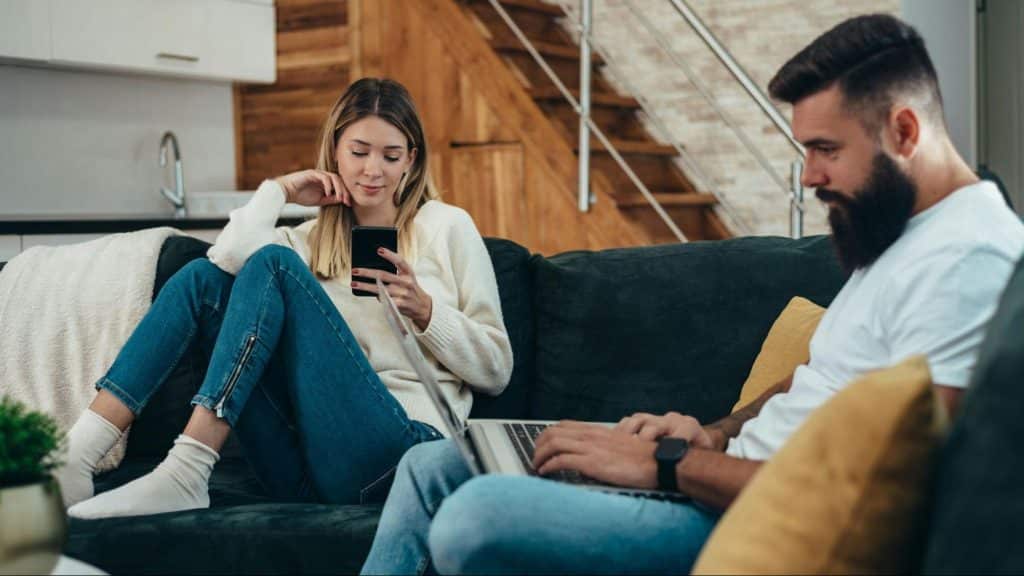 A woman busy with her phone and a man busy with his laptop