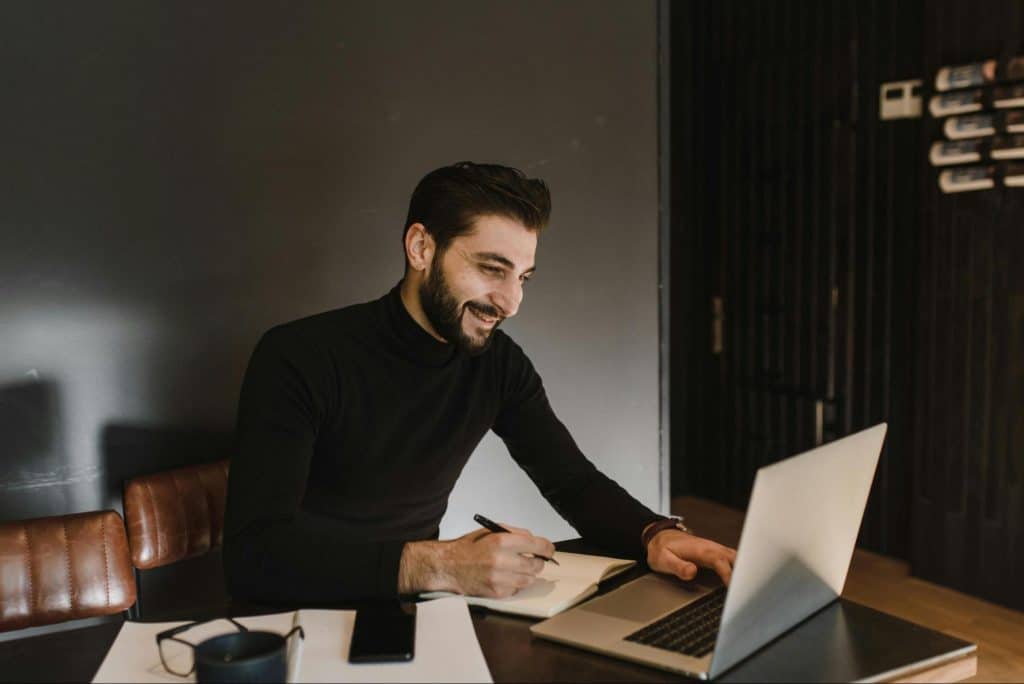 A man smiling while in front of his laptop