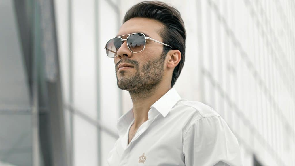 A lightly bearded man wearing sunglasses and looking into the distance.
