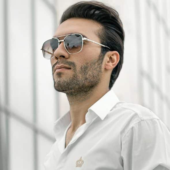 A lightly bearded man wearing sunglasses and looking into the distance.