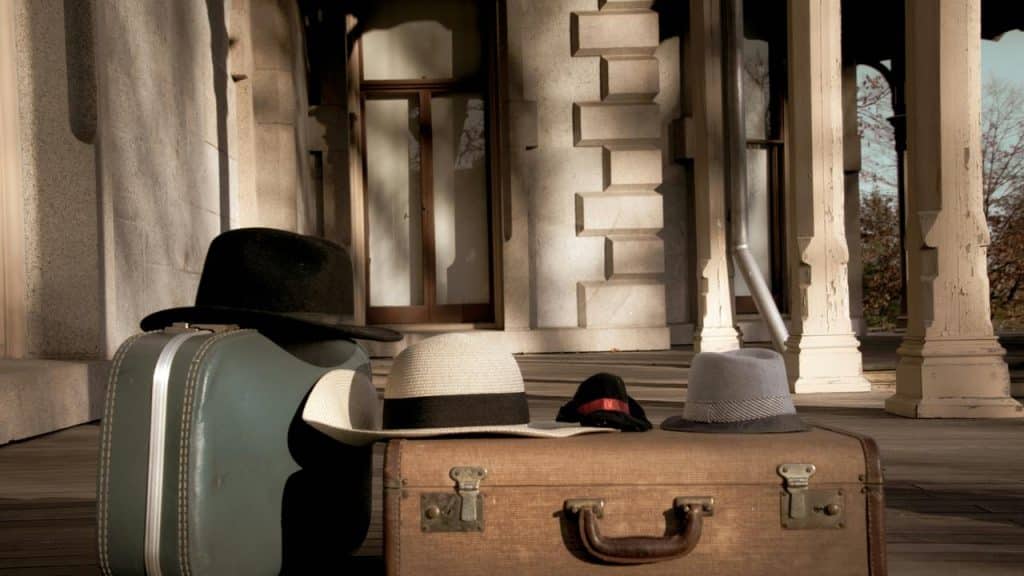 A pair of vintage suitcases with hats on a porch.