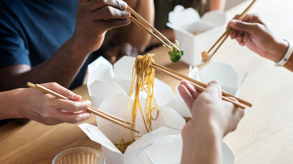 A group of people eating takeout food with chopsticks.