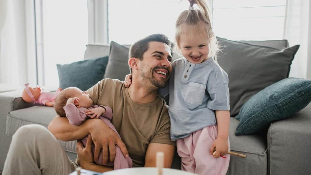A father holding a baby and laughing with his older child.