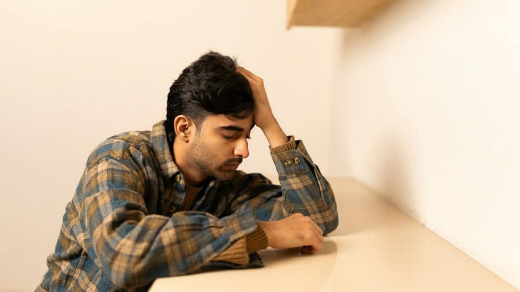A man in a plaid shirt rests his head on his hand while leaning on a table.