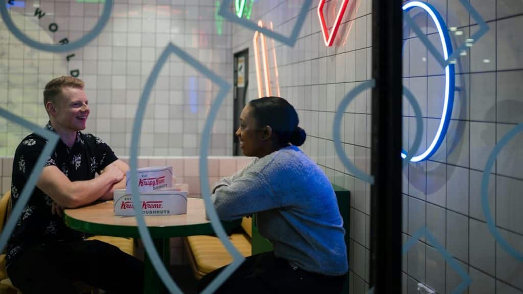 A couple smiling and talking while sitting at a table in a cafe.