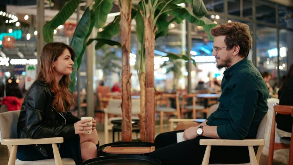 A man and woman sit opposite each other holding mugs in a similar pose.