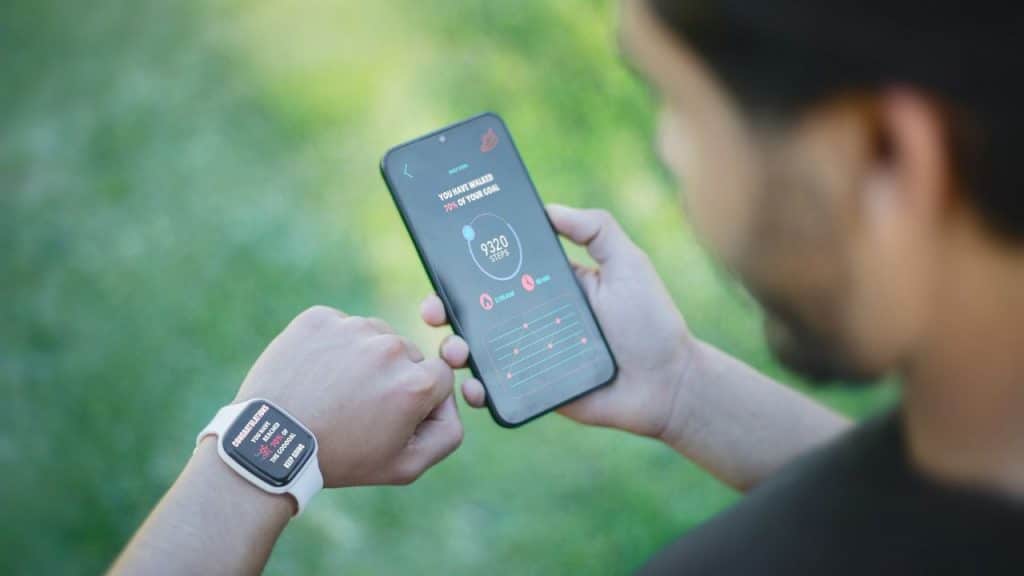A person outdoors looks at a fitness app on a smartphone and a smartwatch.