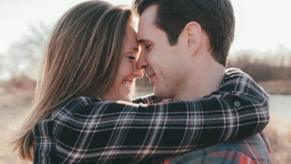 A couple embracing closely outdoors while smiling at each other.