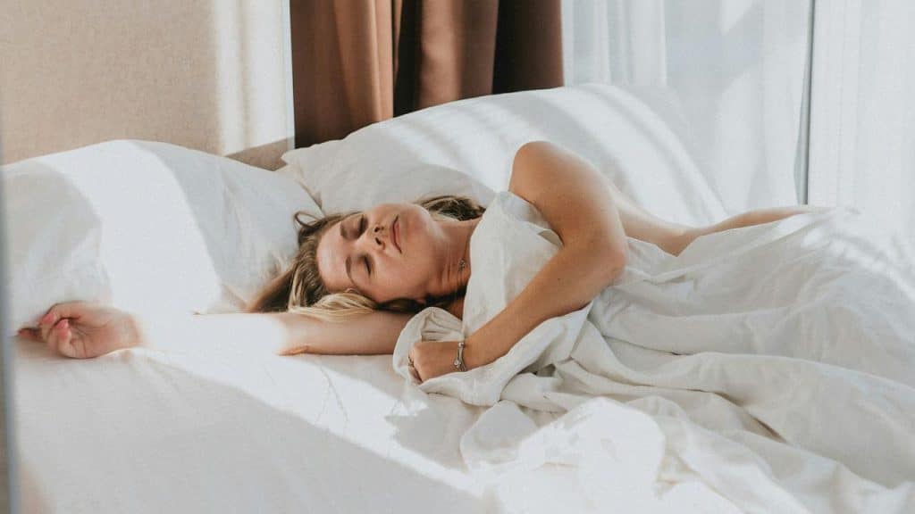 A woman sleeping peacefully in a sunlit bed.