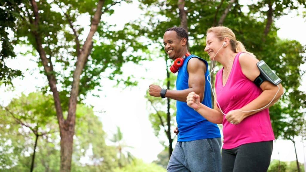 A happy, diverse couple is jogging together through a beautiful park.