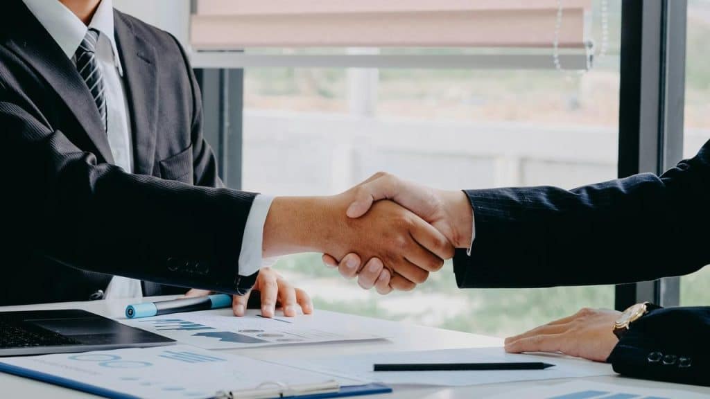 A close-up of two people in business suits shaking hands over documents.