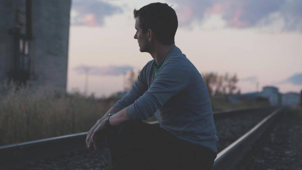 A man sitting on railway tracks, gazing into the distance at dusk.