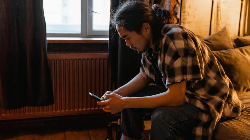 A man sitting on a bed looking at his phone.