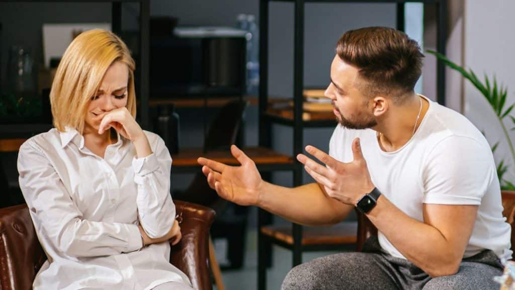 A man gestures with open hands while speaking to a woman who is crying.