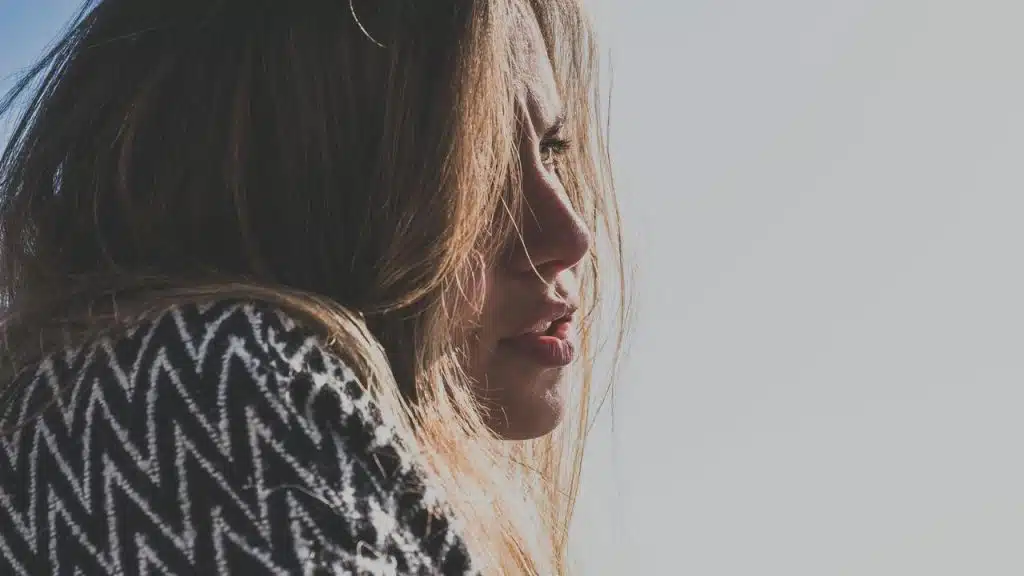 A close-up side profile of a person with long hair, gazing into bright light.