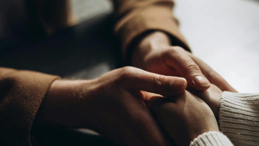 A close-up of two people holding hands gently.