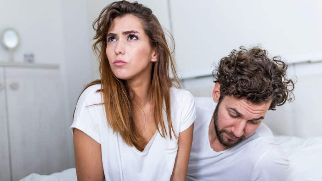 A woman looks upward with a frown while a man with curly hair looks down.