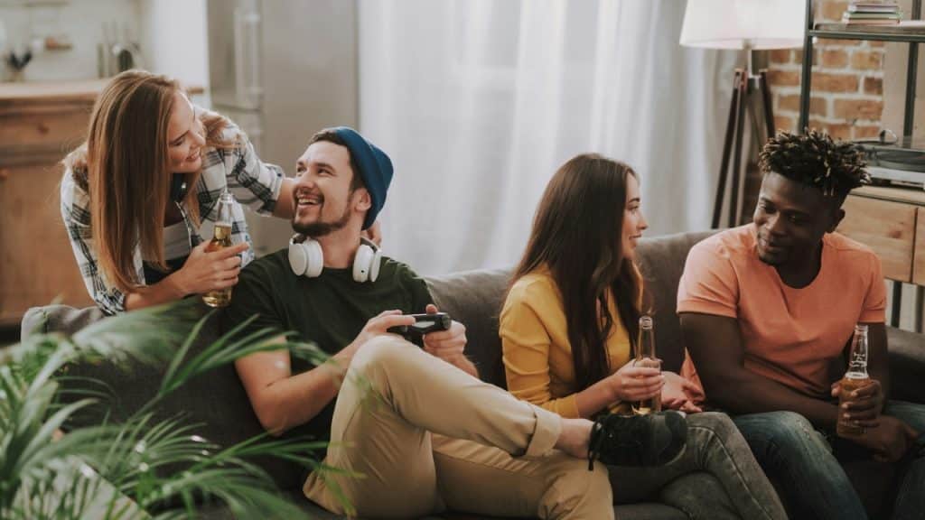 A group of friends talks and laughs while sitting on a sofa with drinks.