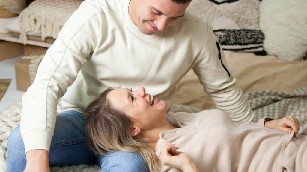 A couple laughing together while relaxing on the floor at home.