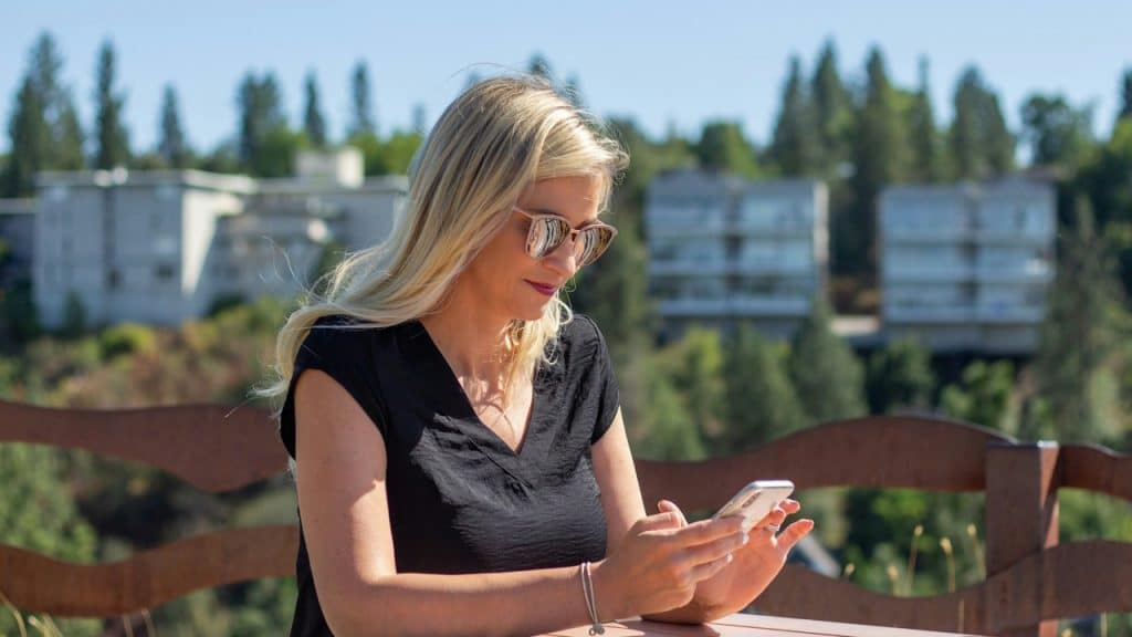 A woman wearing sunglasses looking at her phone while using her phone.