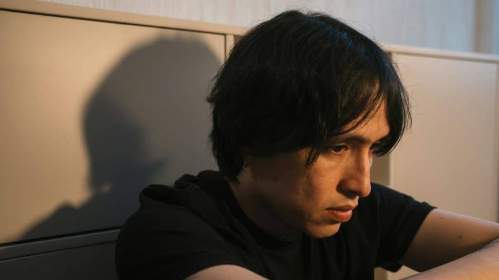 A man with dark hair in a black shirt sits while looking off to the side.