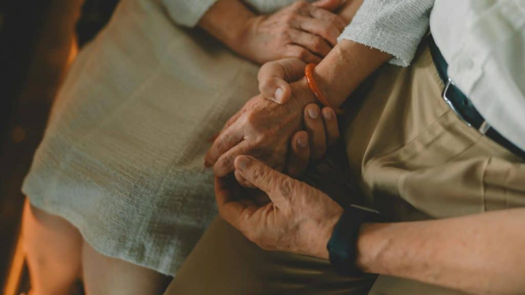 A close-up of two older adults gently holding hands while sitting together.