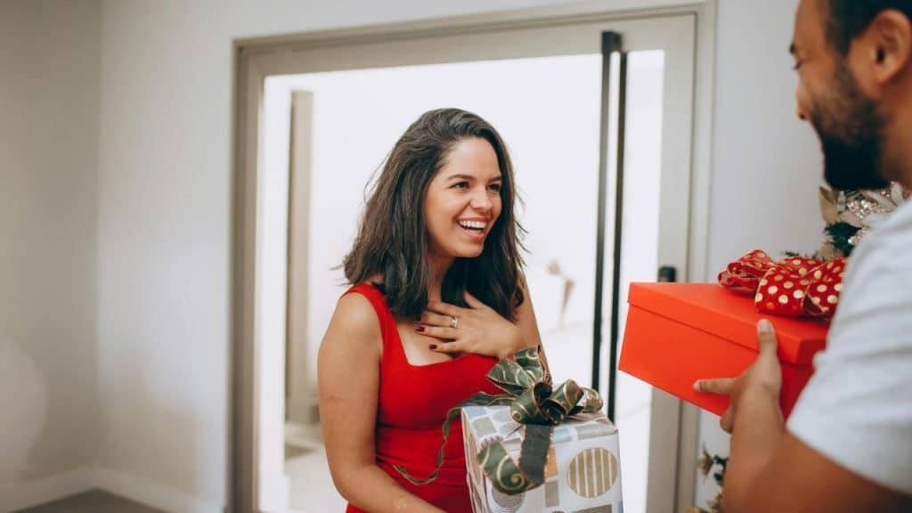 A smiling woman in a red dress receives gifts from a man in a white shirt.