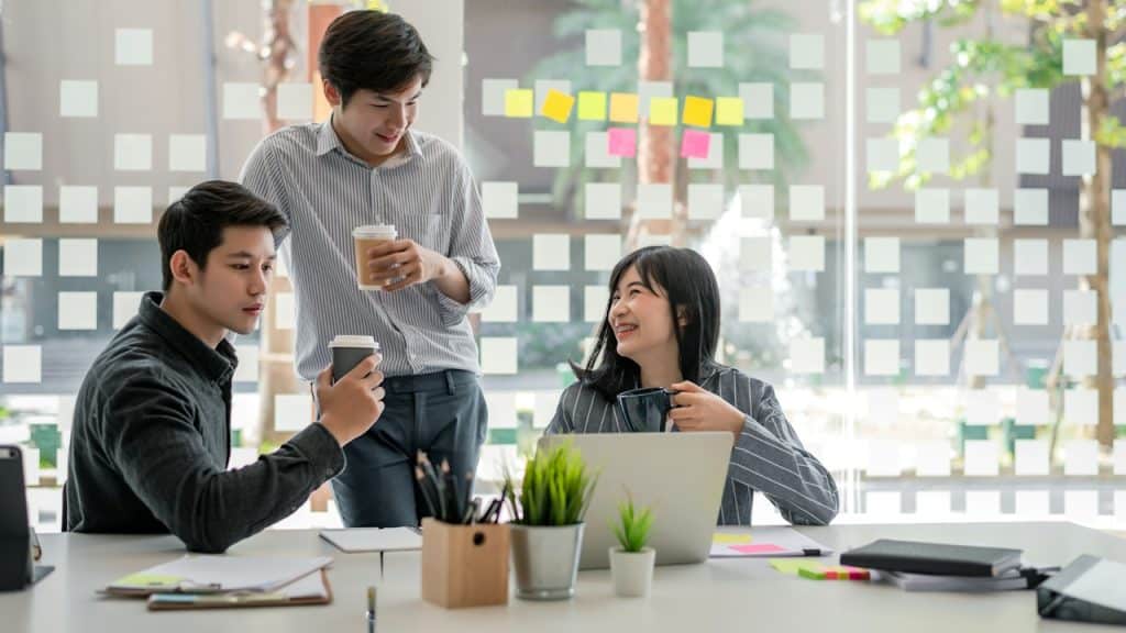 A group of people having coffee and looking at a laptop screen in an office.