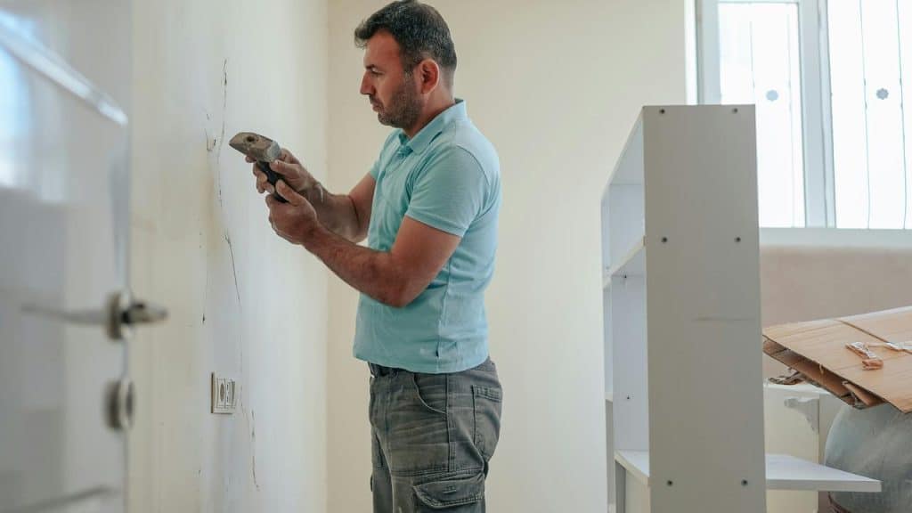 A man using a hammer to work on a wall indoors.