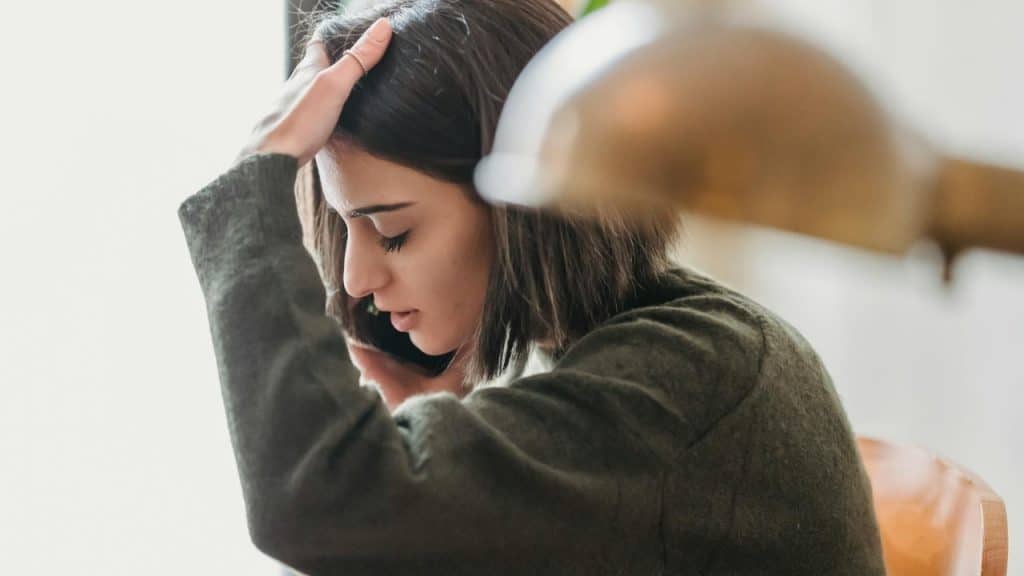 A woman in a green sweater holds a phone to her ear with one hand raised.